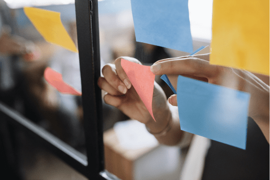 Hand placing multicolored sticky notes on glass wall